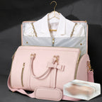 A pink structured duffel bag with gold-tone hardware and a shoulder strap, shown in front of a matching garment bag containing a white collared shirt. A small clear plastic case sits in the lower right on a dark studio background.